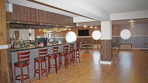 Eine Bar mit Holzwandverkleidung, einer Theke mit Flaschen und mehreren roten Barhocker.