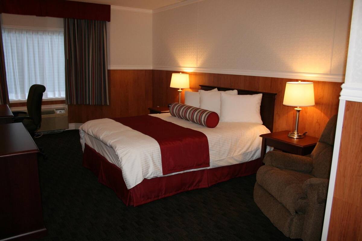 Ein Hotelzimmer mit einem großen Bett, zwei Nachttischen mit Lampen, einem Holz-Kopfteil, einem Schreibtisch und einem Stuhl.