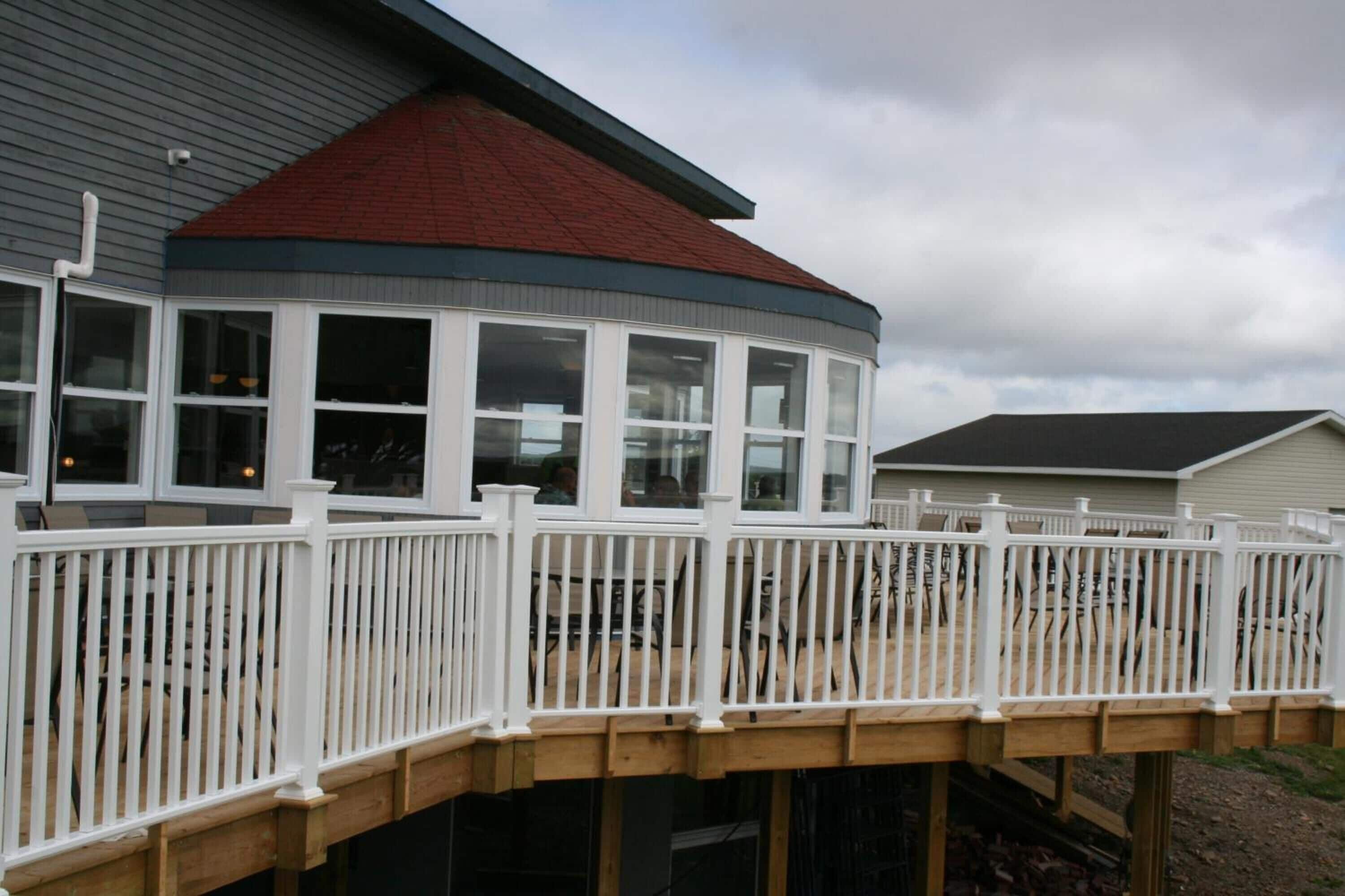 A covered outdoor deck with white railings and a curved glass enclosure.