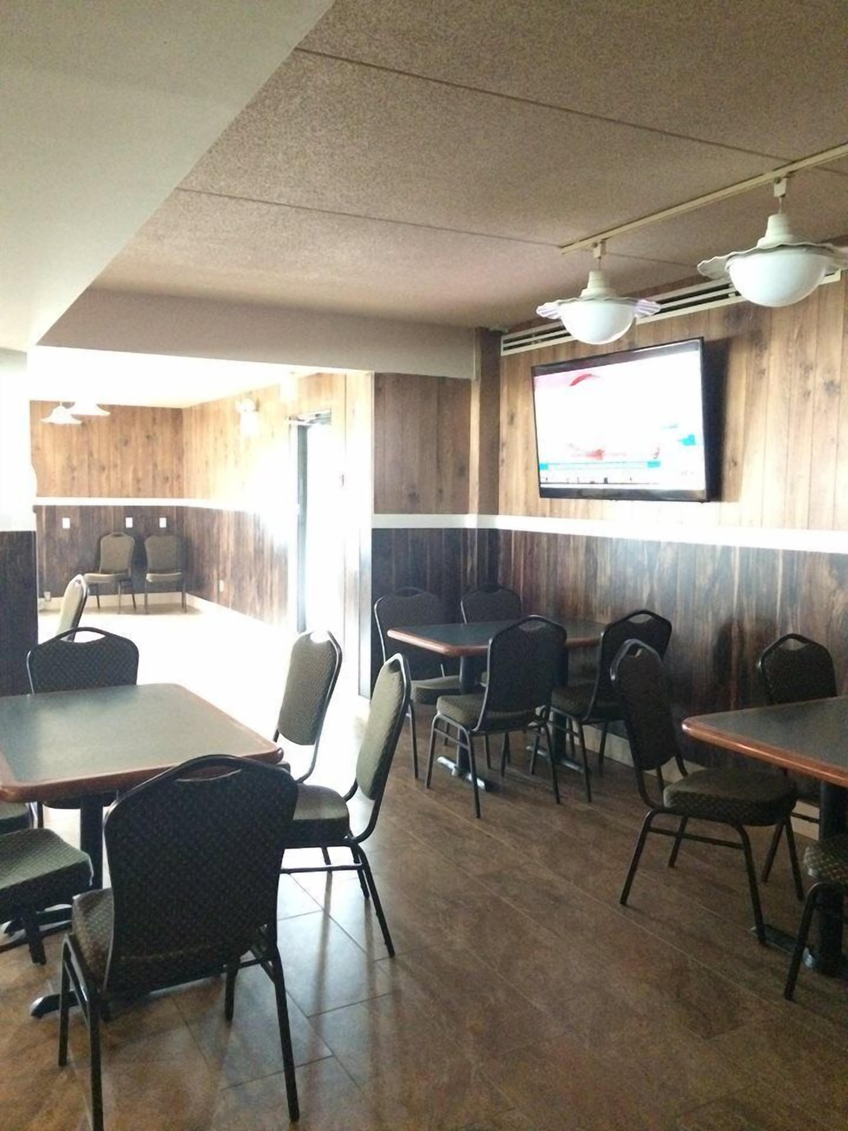 A restaurant with wooden walls, multiple tables and chairs, and a TV mounted on the wall.