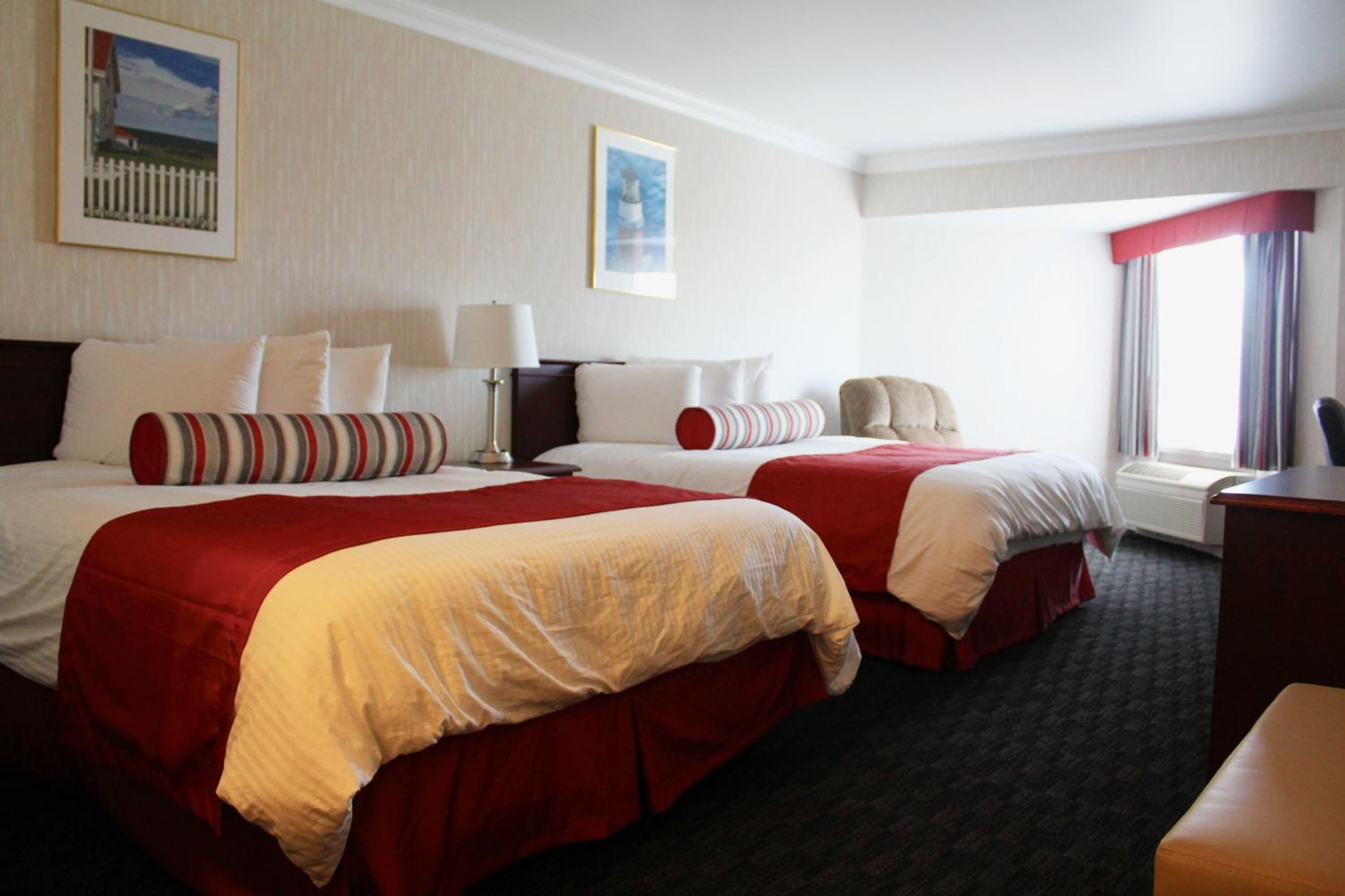 Une chambre d’hôtel avec deux lits, chacun agrémenté de draps rouges et blancs, un bureau et une chaise.