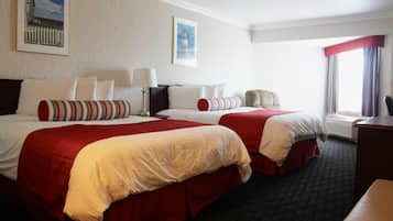 A hotel room with two beds, each with red and white bedding, a desk, and a chair.