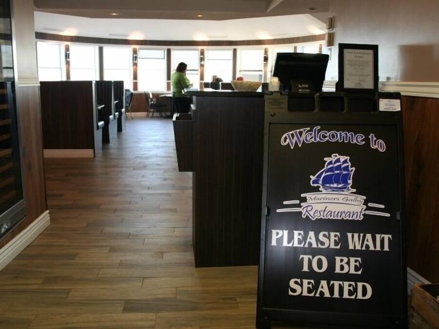 Interior de un restaurante con mostrador de recepción, piso de madera y vistas al comedor.