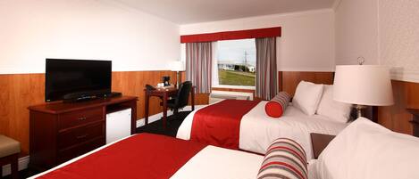 A hotel room with two beds, a TV, a desk, and a window with a view.