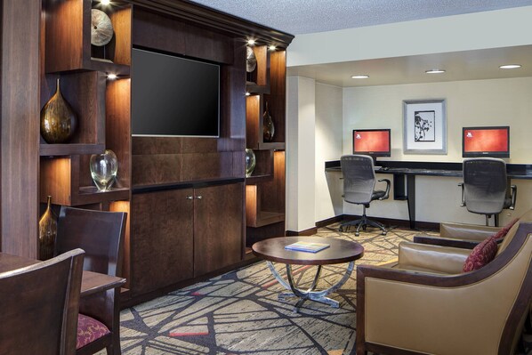 A hotel lounge with a TV, two monitors, comfortable seating, and decorative vases. - Houston Marriott Uptown by the Galleria (Houston)