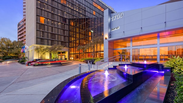 A modern hotel with a prominent address sign, a well-lit entrance, and a landscaped outdoor area with a water feature. - Houston Marriott Uptown by the Galleria (Houston)