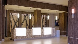A reception area with a modern design, featuring a reception desk, pendant lighting, and a patterned wall. - Houston Marriott Uptown by the Galleria (Houston)