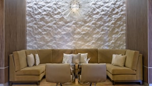 A modern living room with a sectional sofa, two armchairs, a glass coffee table, and a geometric patterned wall. - Houston Marriott Uptown by the Galleria (Houston)