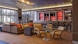 A spacious lobby with a seating area, a bar with red lighting, and large windows. - Houston Marriott Uptown by the Galleria (Houston)