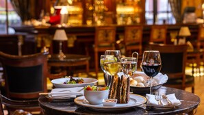 Una mesa de comedor con ensalada, sándwiches, copas de vino y una cesta de pan en un restaurante con cálida iluminación.