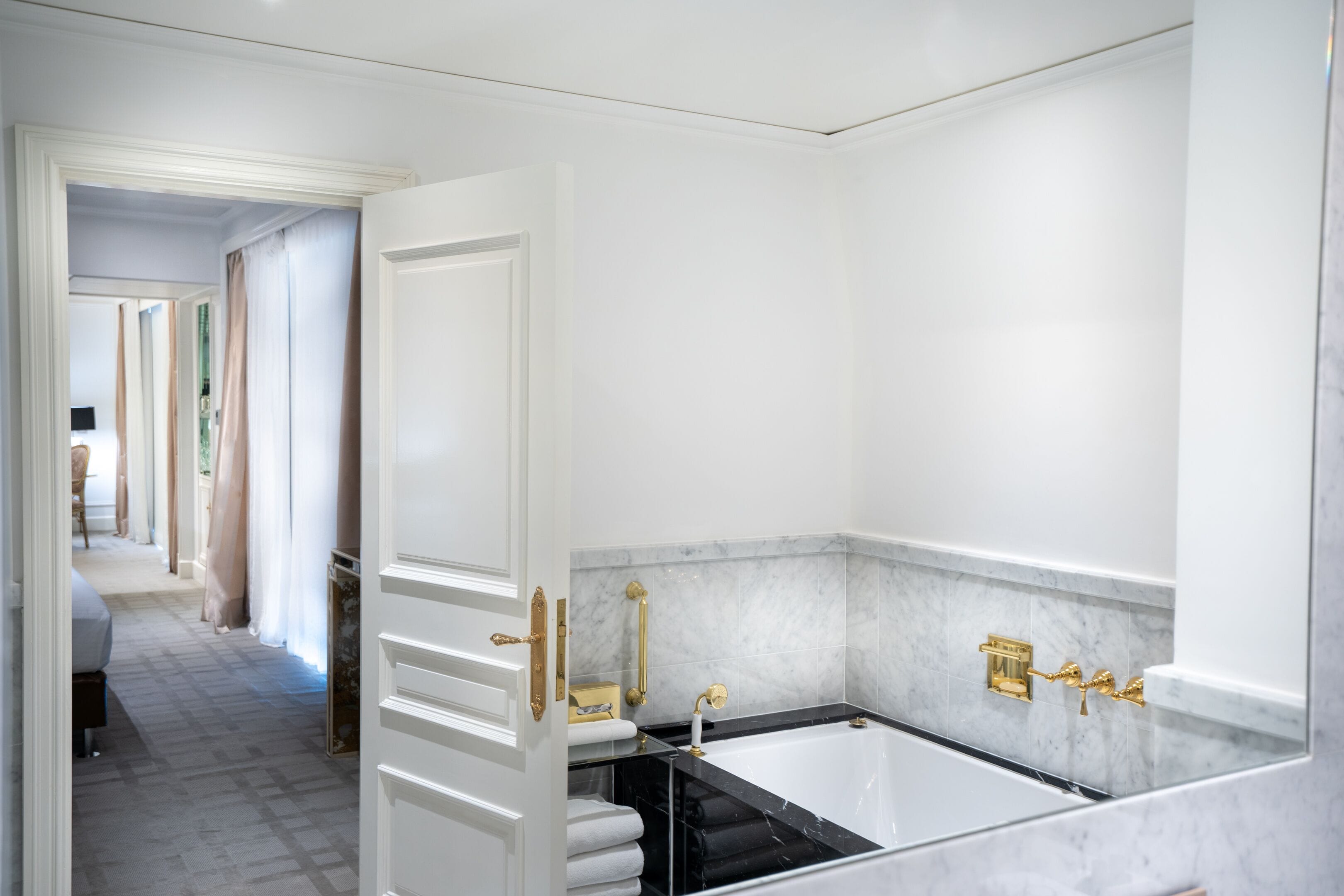 Un baño moderno con una bañera grande, paredes de mármol y detalles dorados.