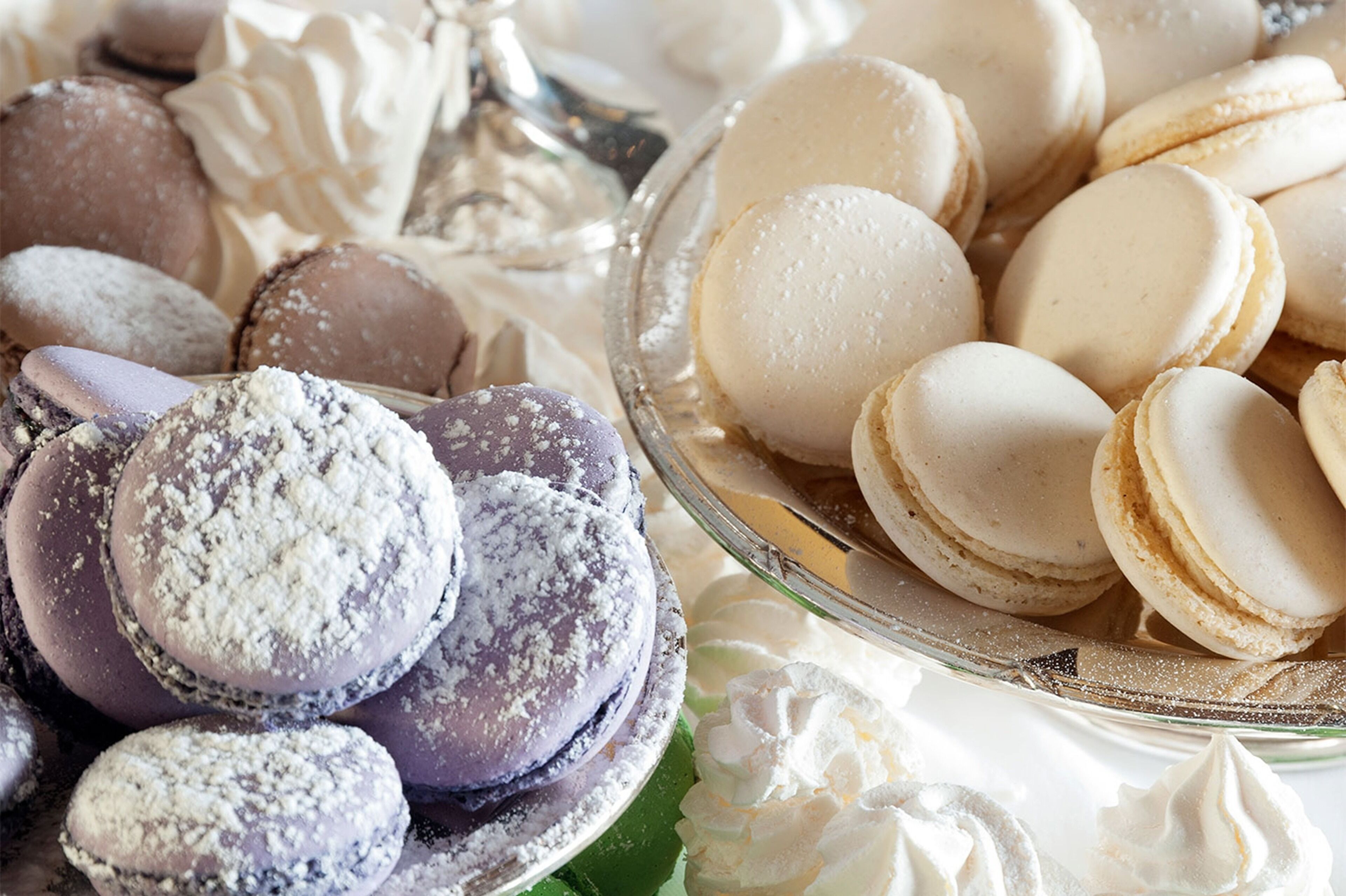 Une variété de macarons présentés sur une assiette en verre, certains saupoudrés de sucre glace.