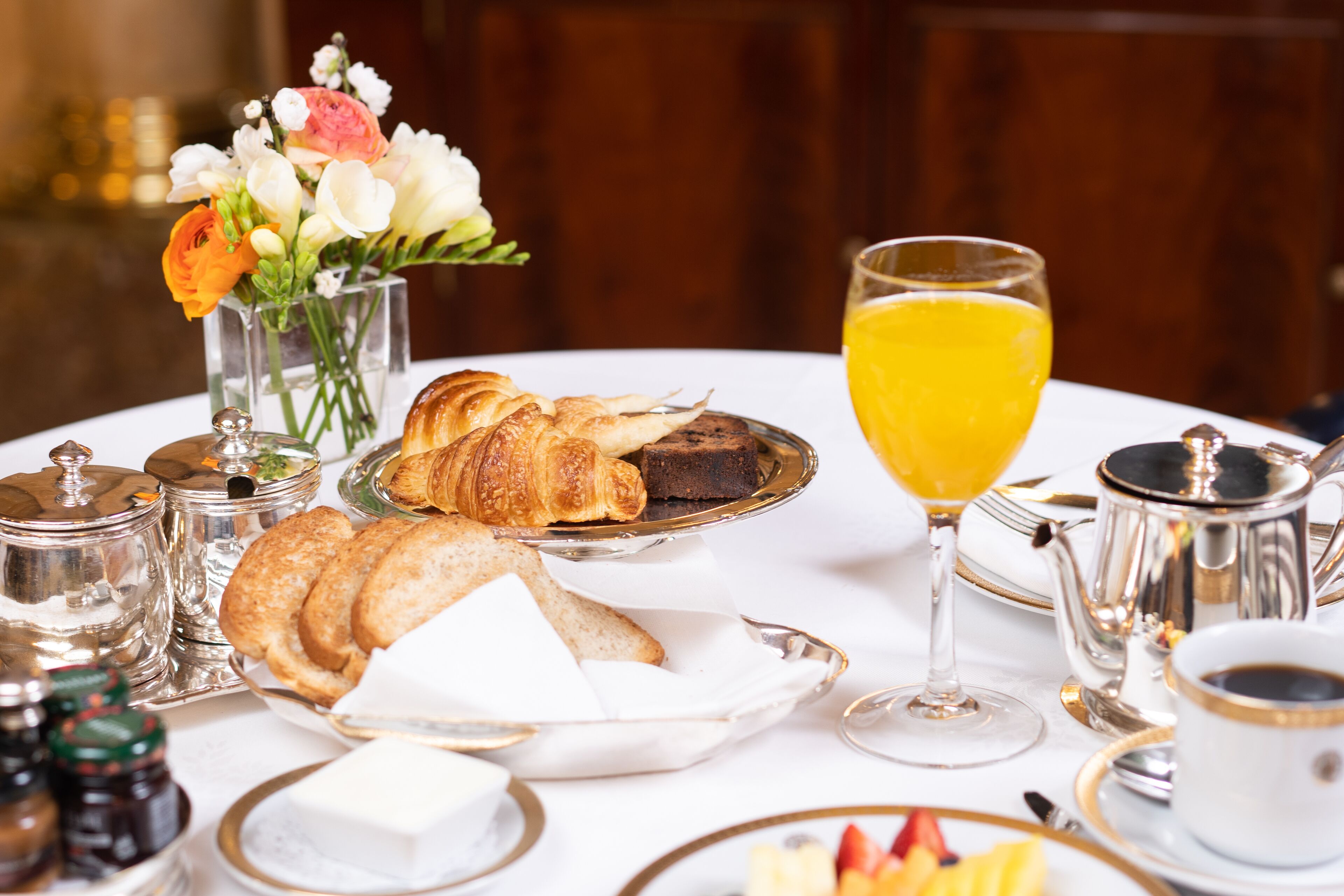 Desayuno con cruasanes, zumo de naranja y un florero con flores.