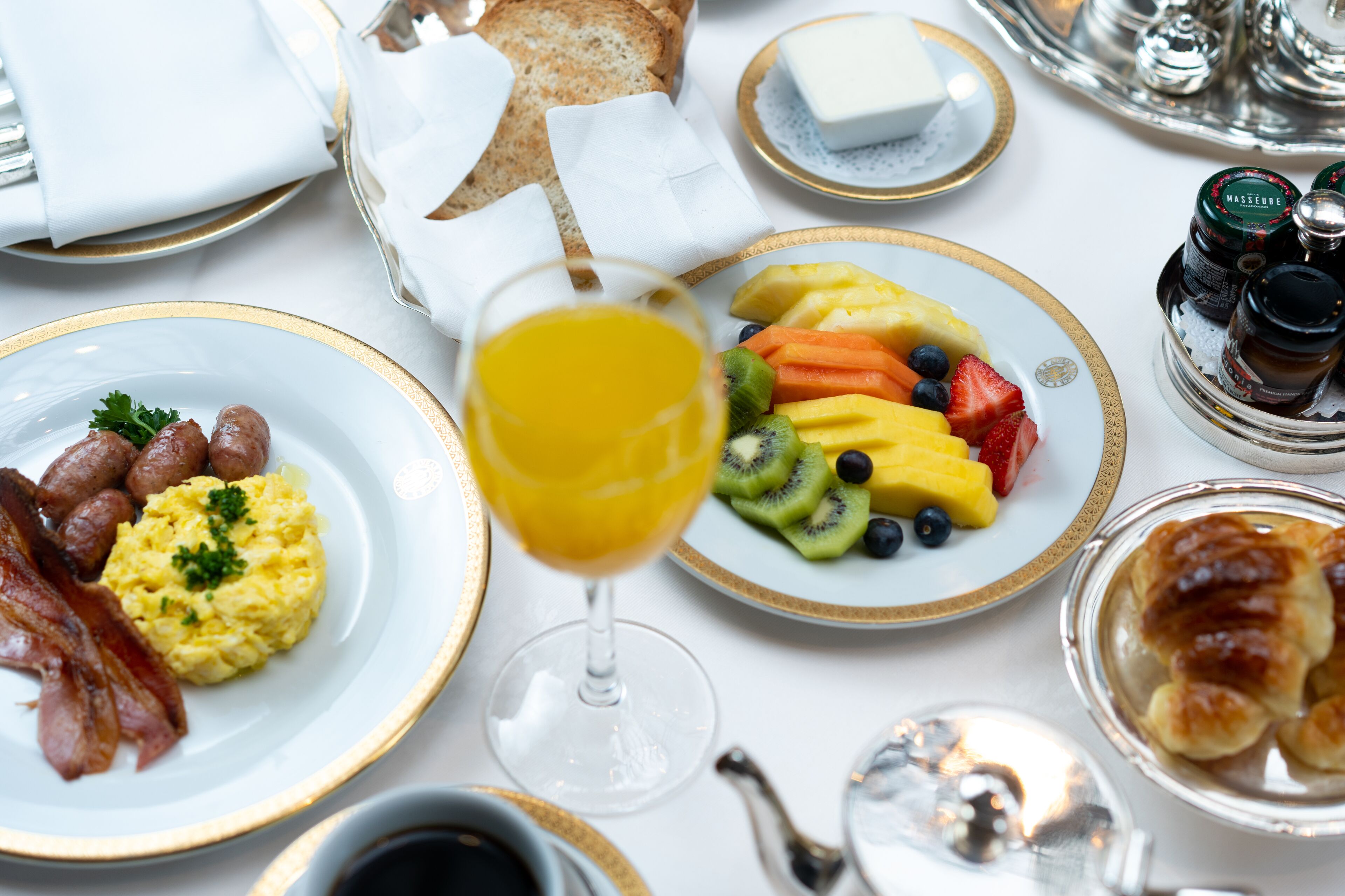 A breakfast setting with plates of eggs, bacon, toast, and fruit.