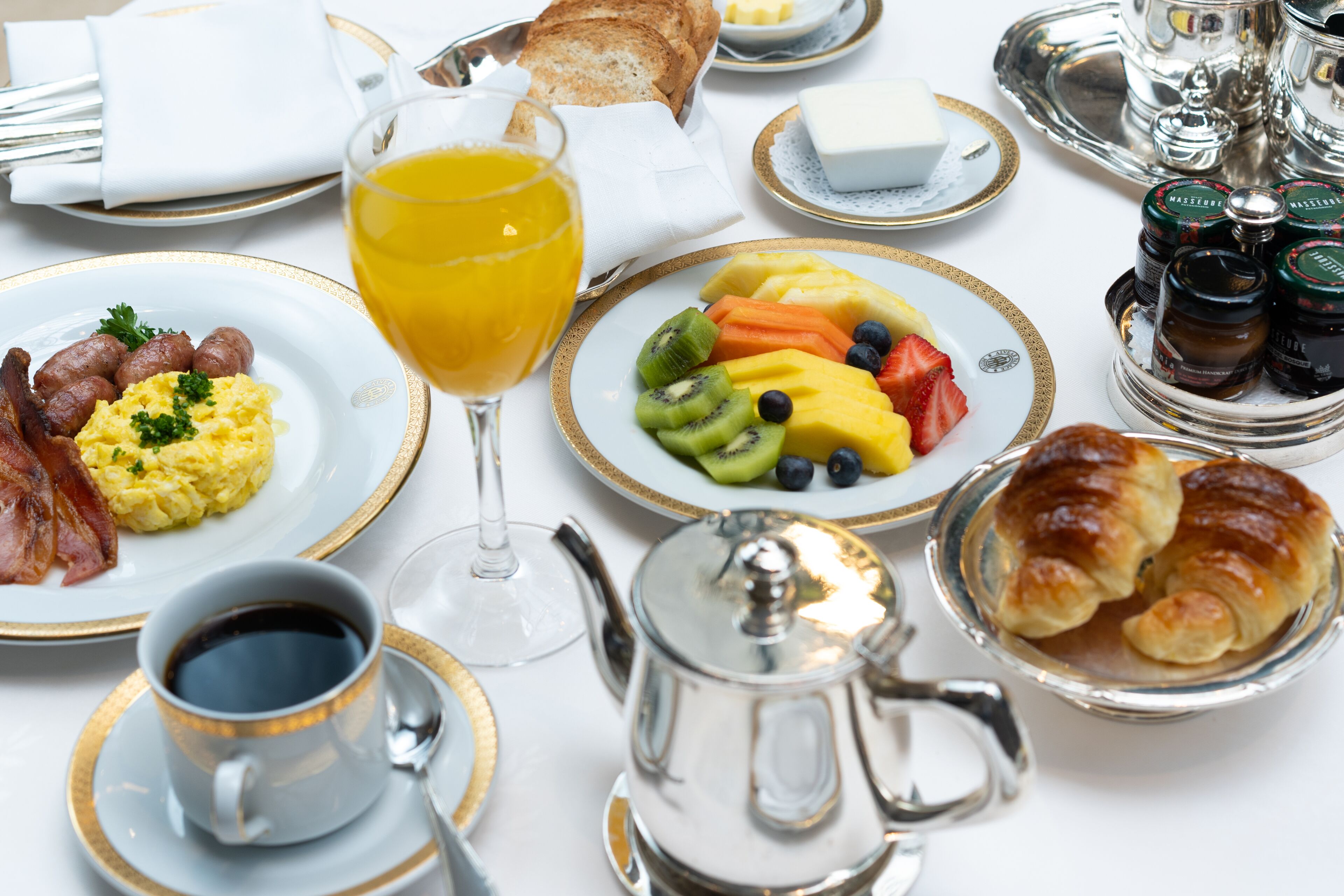 A breakfast setting with plates of food, a glass of orange juice, a teapot, and condiments.