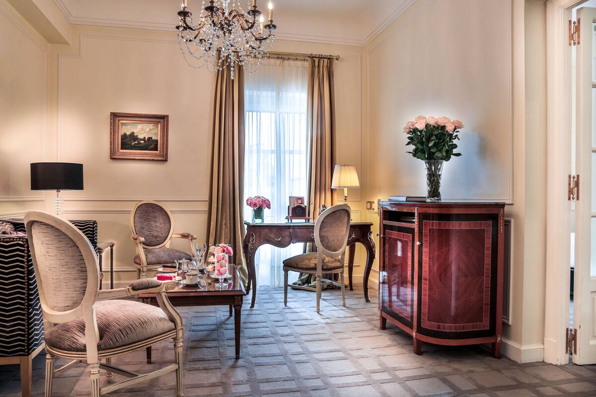 Una habitación con candelabro, una mesa de comedor con sillas, un escritorio con lámpara y un aparador con un jarrón de flores.