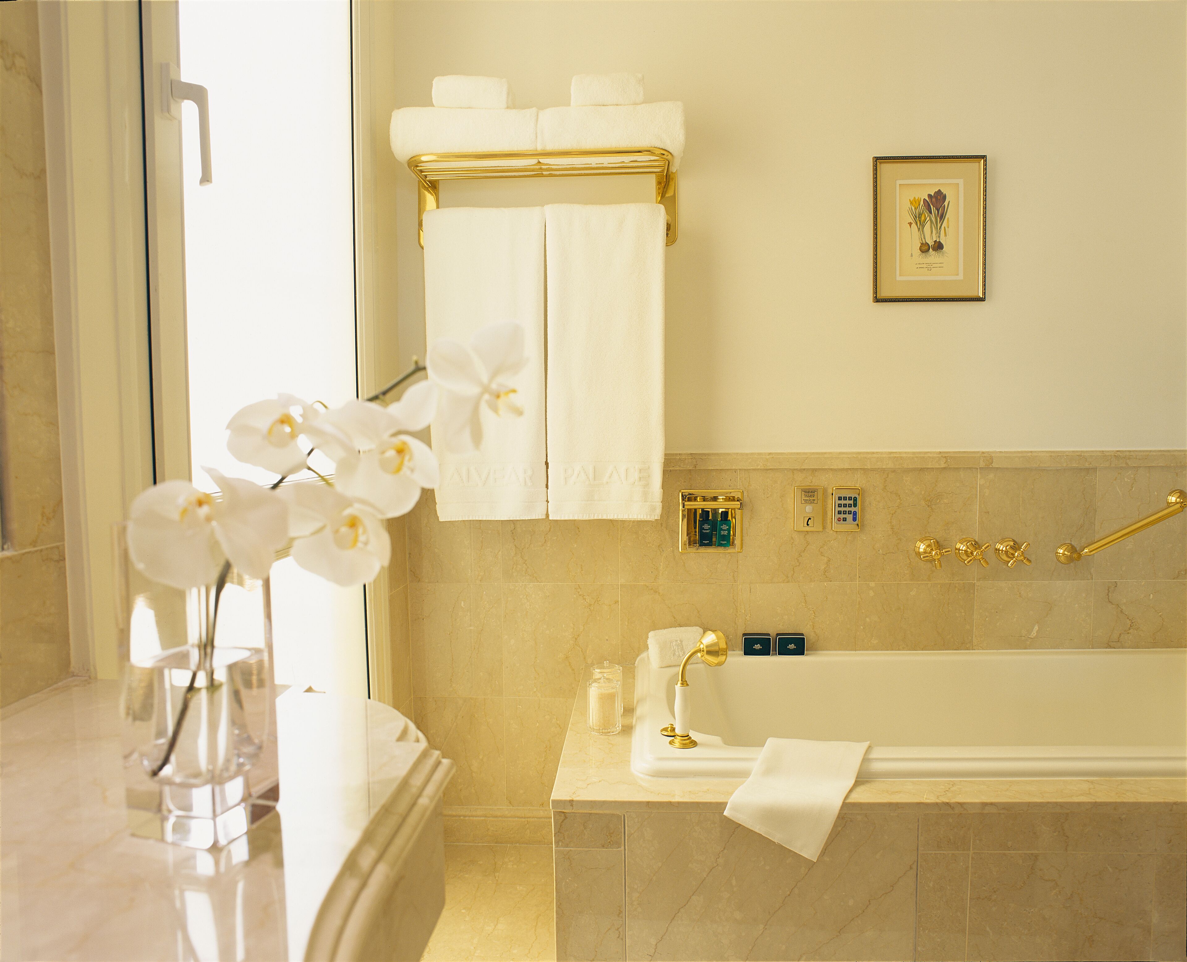 A bathroom with a bathtub, white towels, a framed botanical print, and a vase with white orchids.
