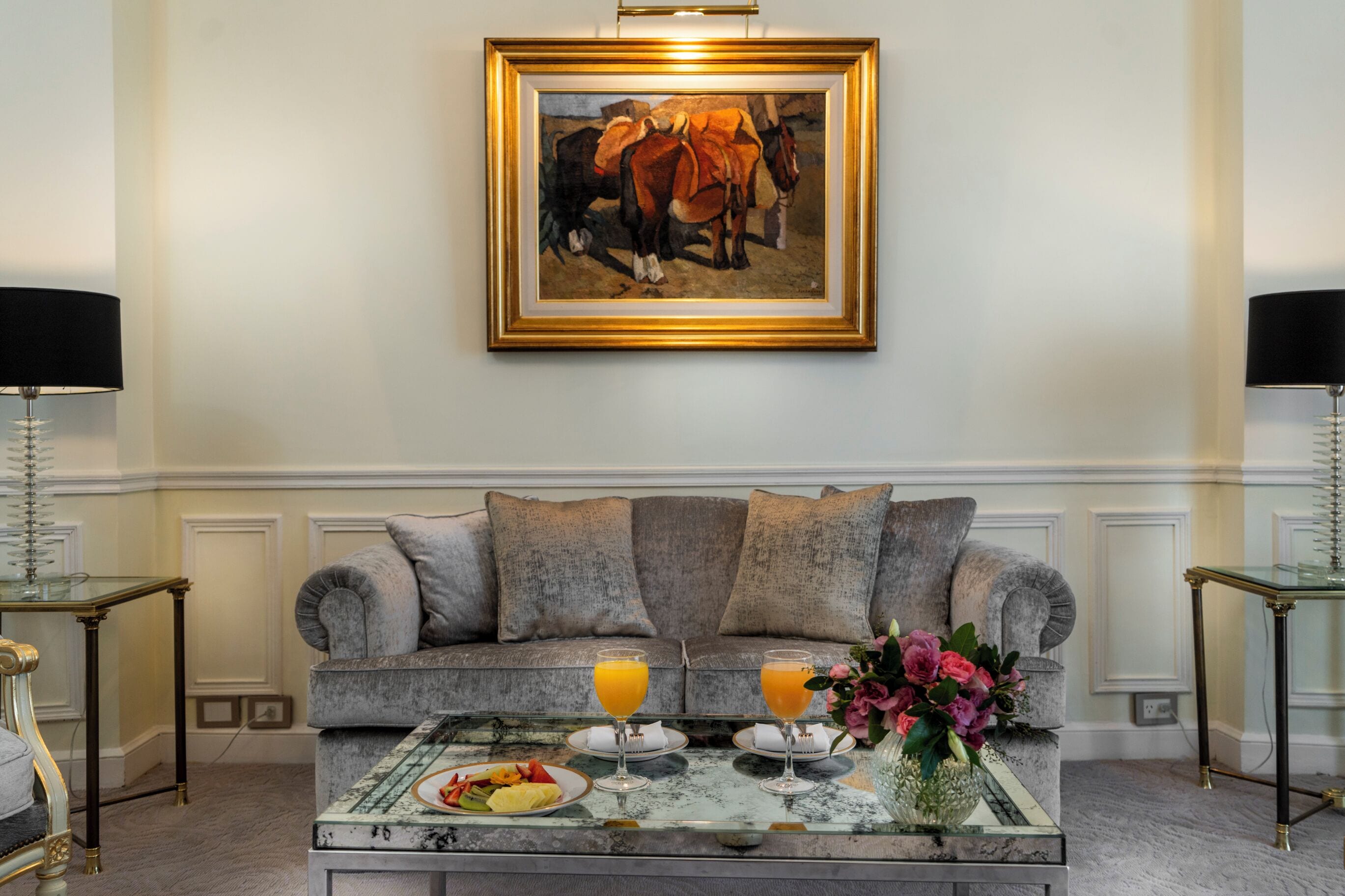 Een woonkamer met een bank, een bijzettafeltje met fruit en drankjes, en een schilderij aan de muur.