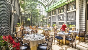 Un comedor interior con mesas redondas, sillas y un techo alto con estructura de vidrio.
