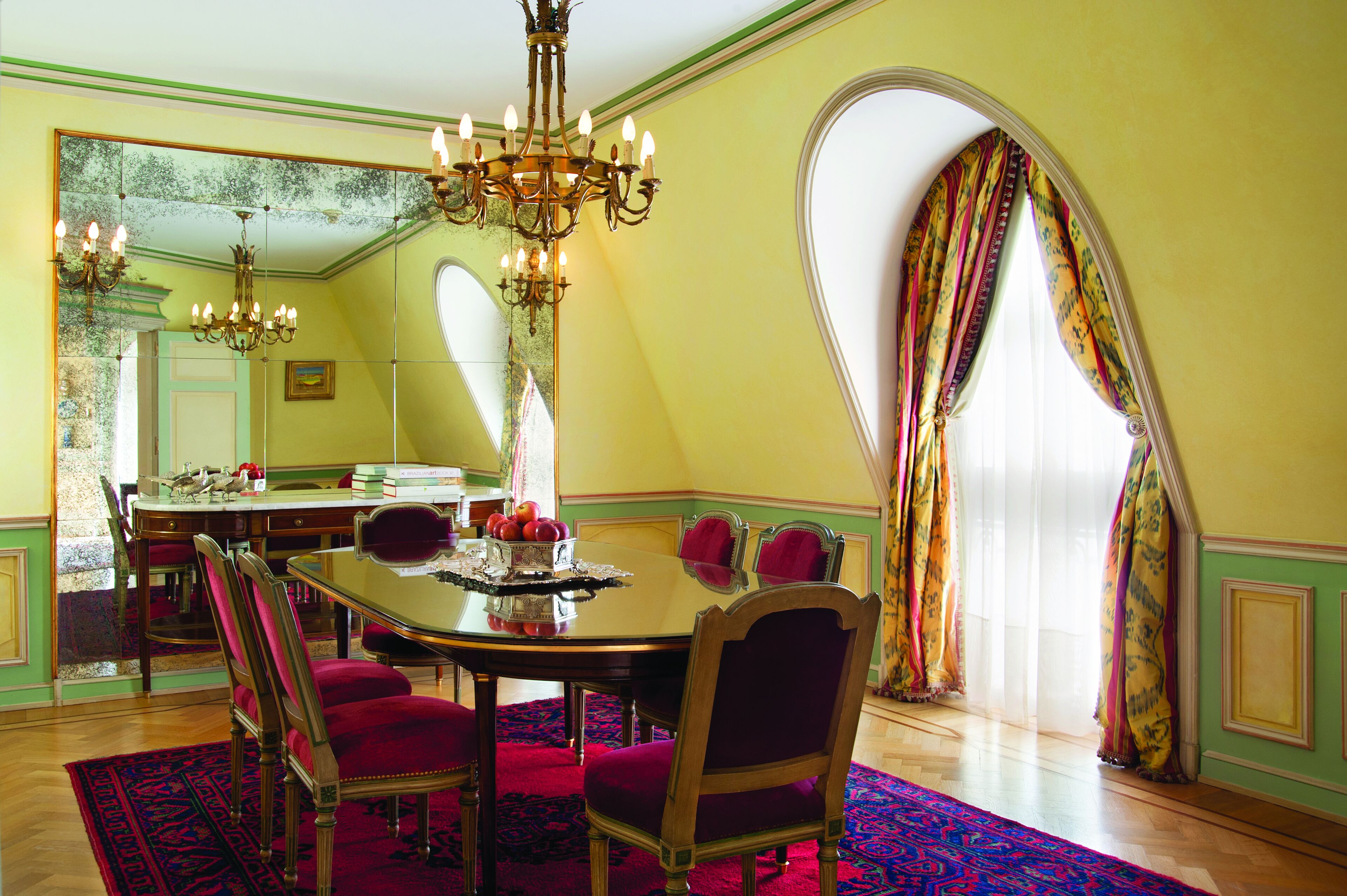 Comedor con una gran lámpara de araña, una mesa de comedor para cuatro comensales y un espejo que refleja la habitación.