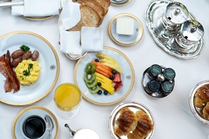 A breakfast setting with plates of eggs, sausages, toast, croissants, and fruit. - Alvear Palace Hotel (Buenos Aires)