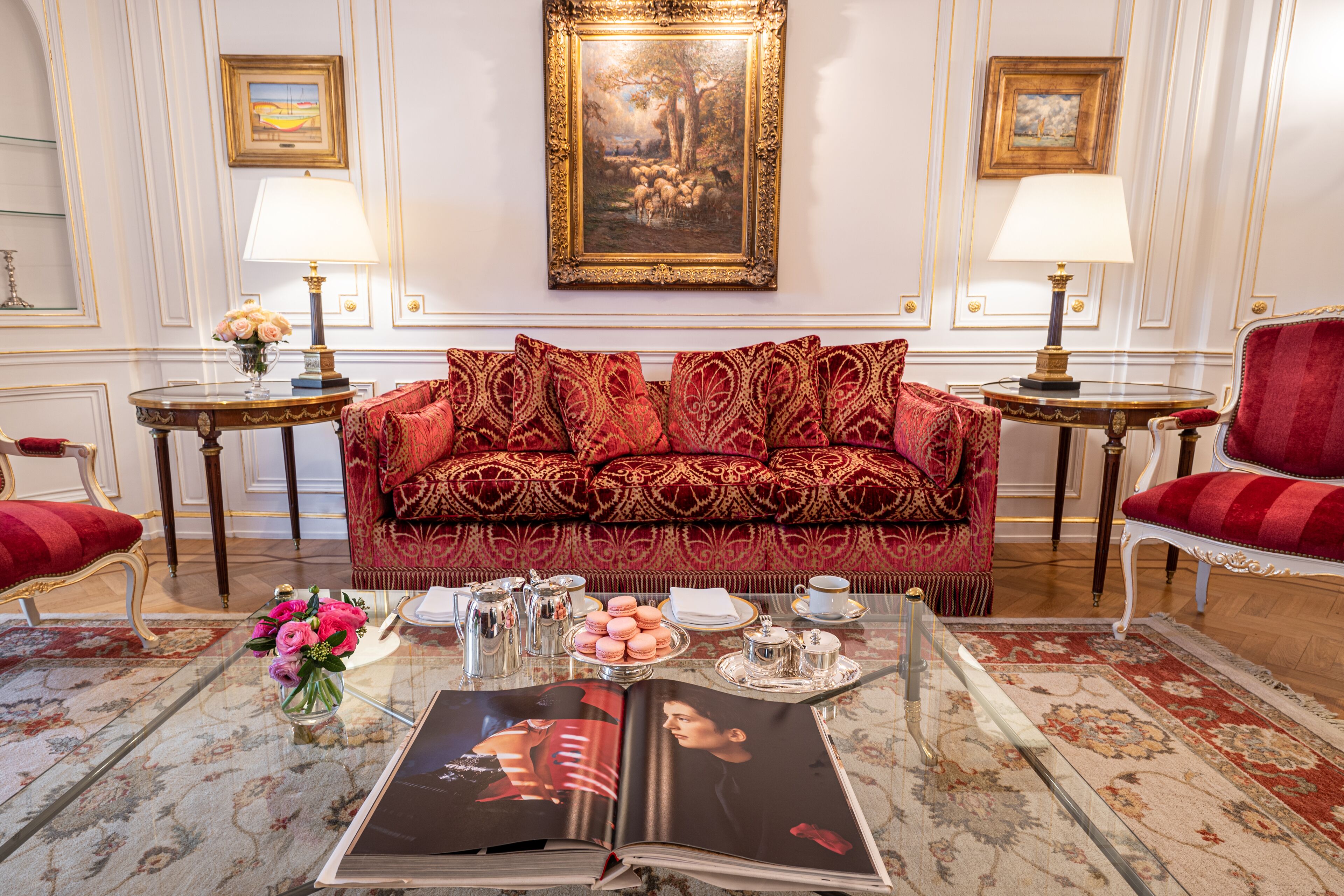 A luxurious room with a red patterned sofa, a coffee table with a magazine, a vase of flowers, and two side tables with lamps.