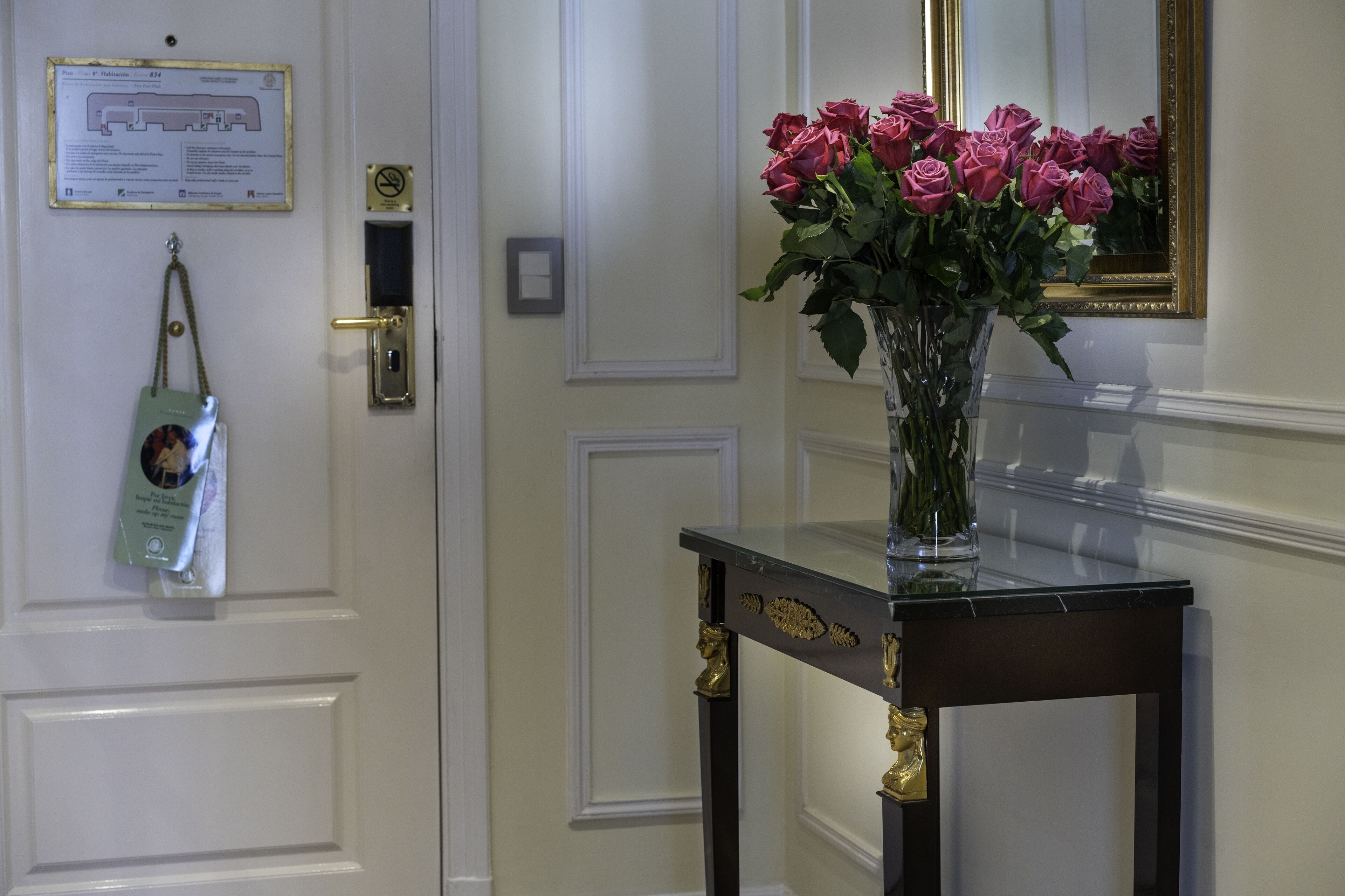 A door with a sign, a keycard holder, and a vase with roses on a console table.