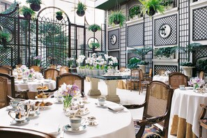 Un comedor formal con mesas redondas, manteles blancos y sillas de mimbre.