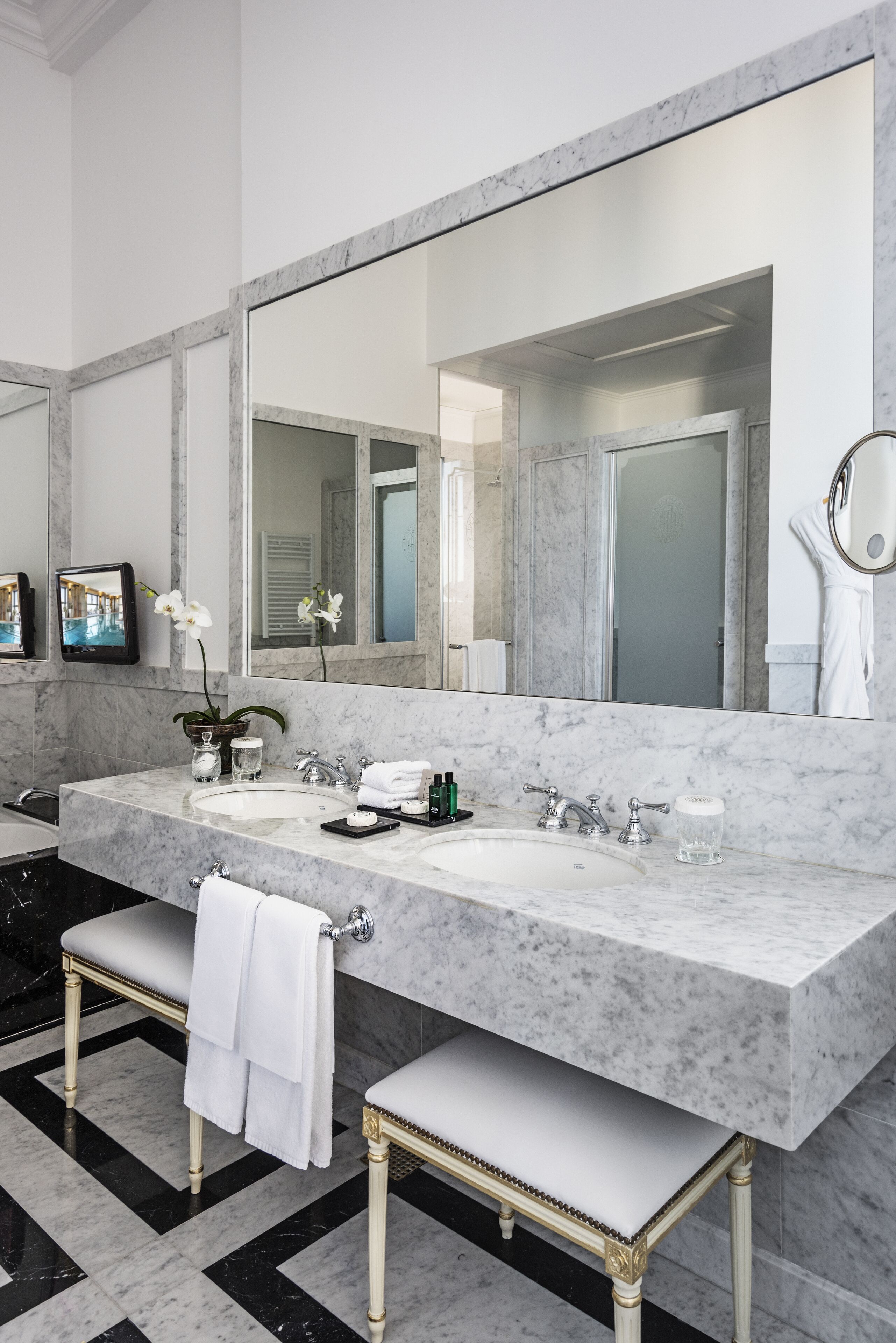 Une salle de bain moderne avec un grand lavabo en marbre, un grand miroir et un banc avec des serviettes.