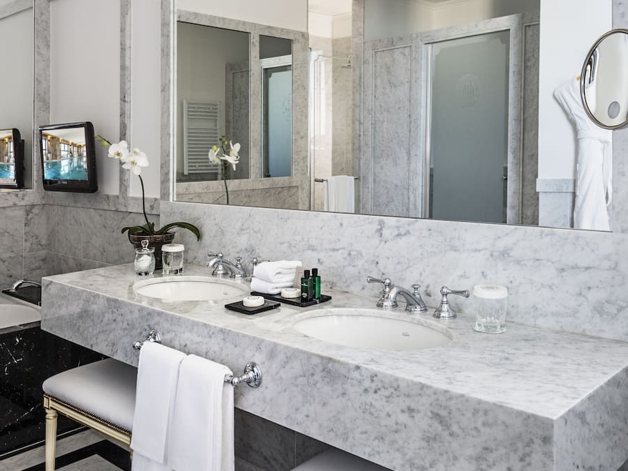 Une salle de bain moderne avec un grand lavabo en marbre, un grand miroir et un banc avec des serviettes.