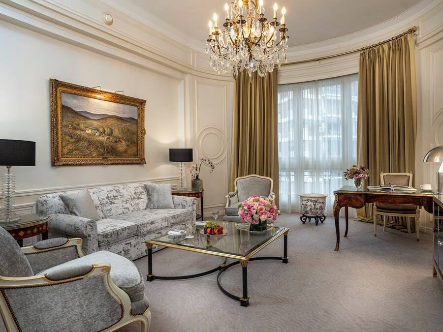 Ein luxuriöses Wohnzimmer mit einer Chandelier, einer Couch, Sesseln, einem Couchtisch und einem Schreibtisch mit einer Lampe.