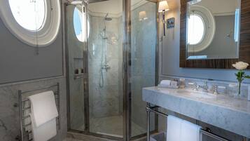 A modern bathroom with a glass-enclosed shower, a marble vanity, a large mirror, and a towel rack.