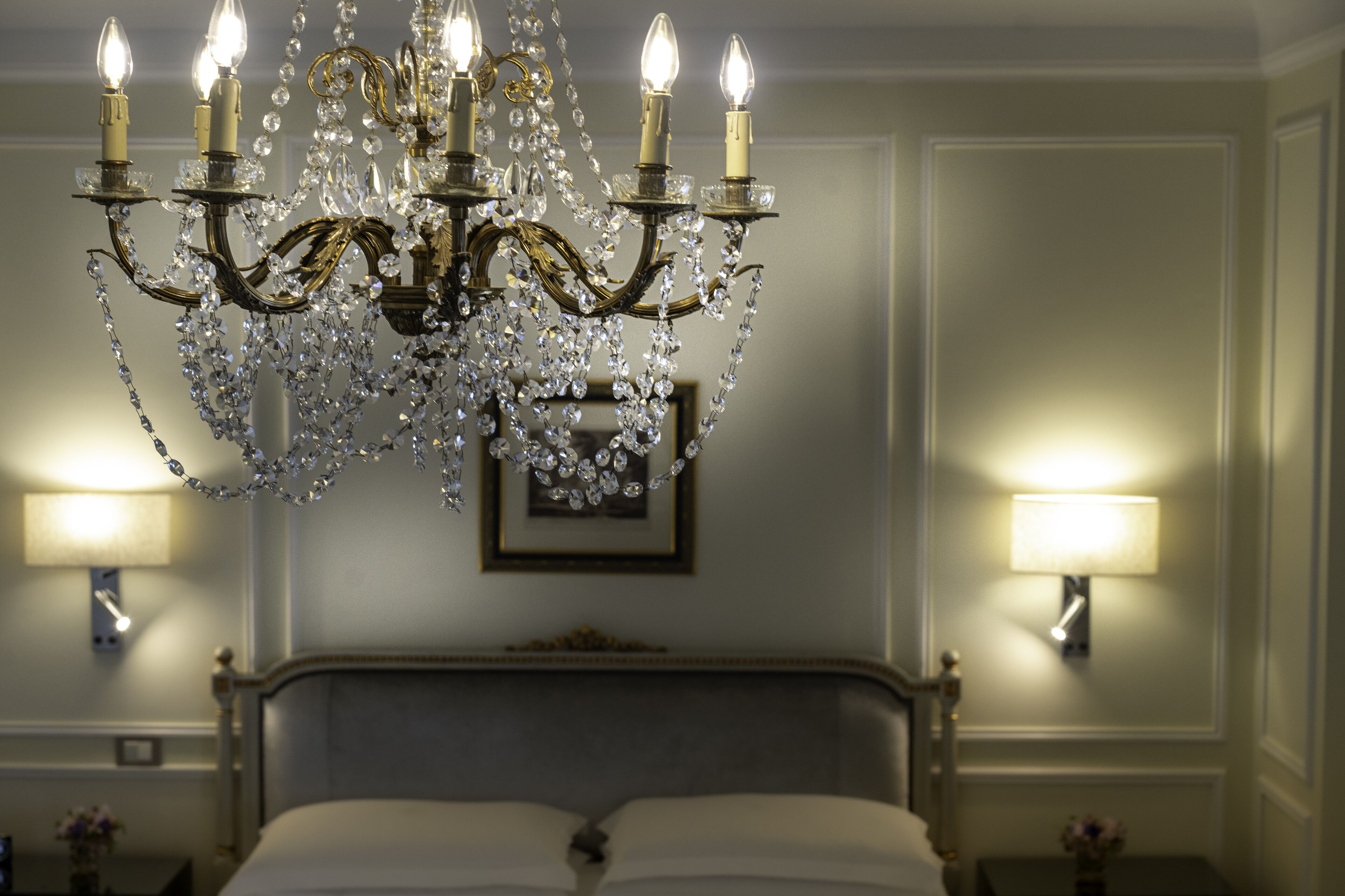 Un candelabro con múltiples luces, una cama y dos lámparas de pared.