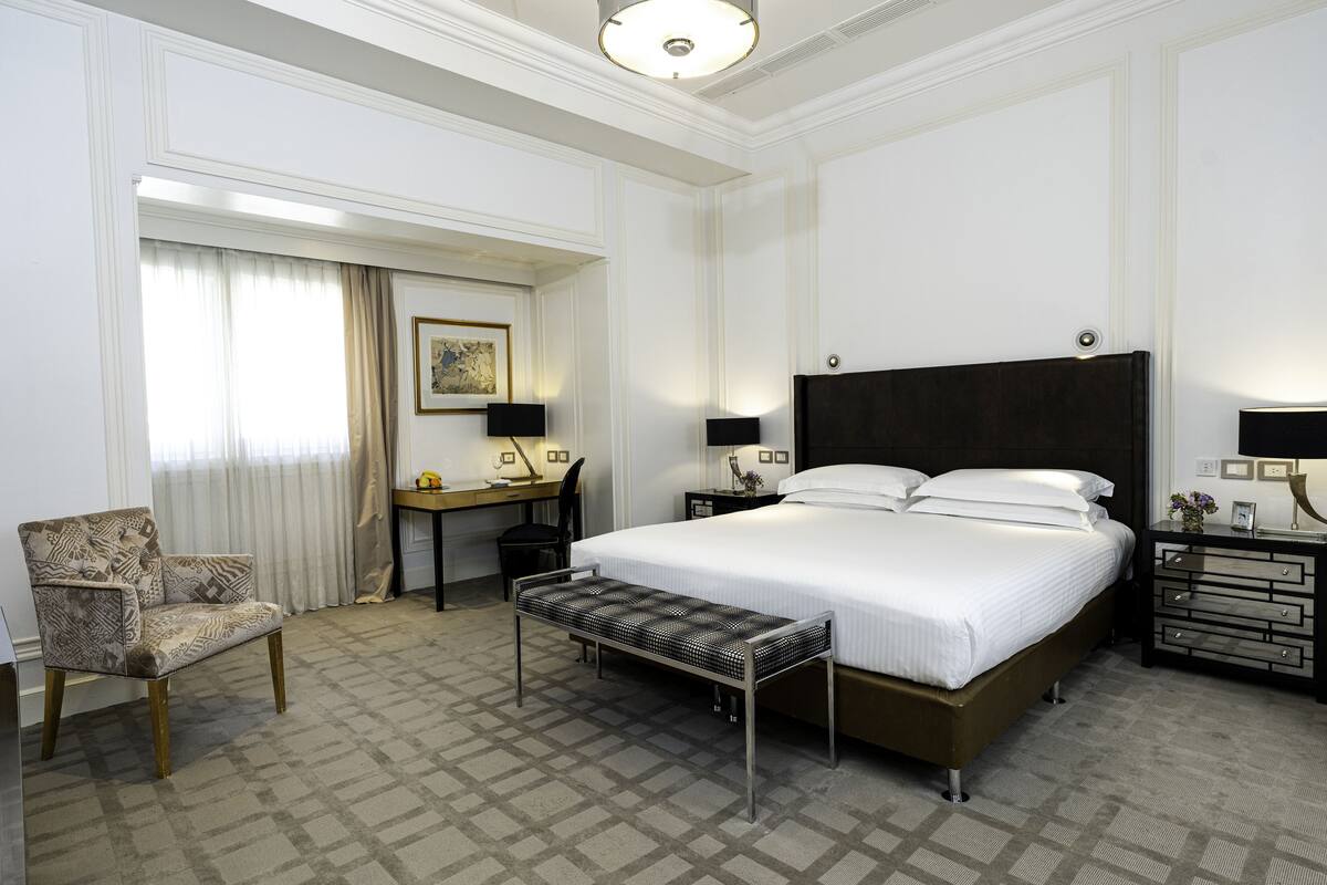 Una habitación de hotel con una cama grande, un escritorio, una silla y un banco.