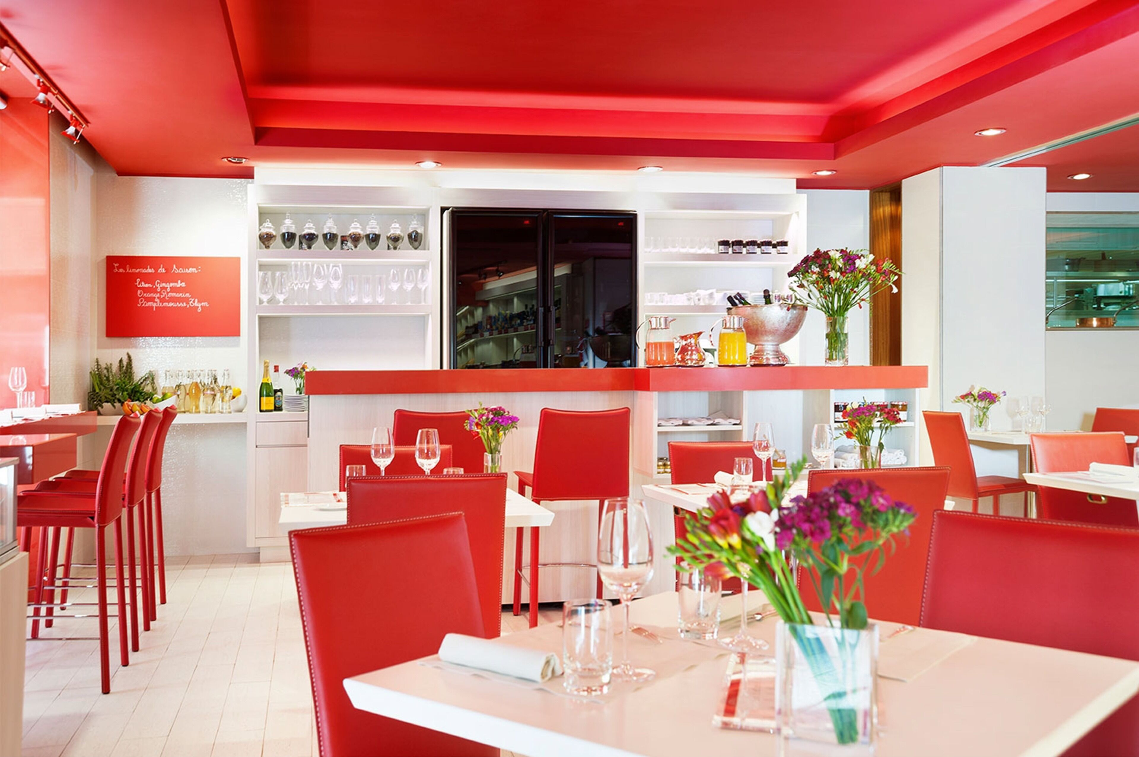 A restaurant with red chairs and tables, a bar area, and a display of wine glasses and bottles.