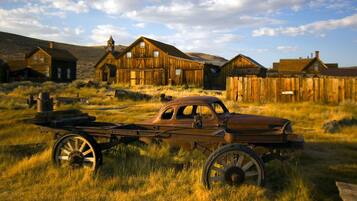 An old wooden building with a large front porch and a vintage car in front.