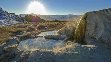 A natural landscape with a hot spring, mountains, and a clear sky.