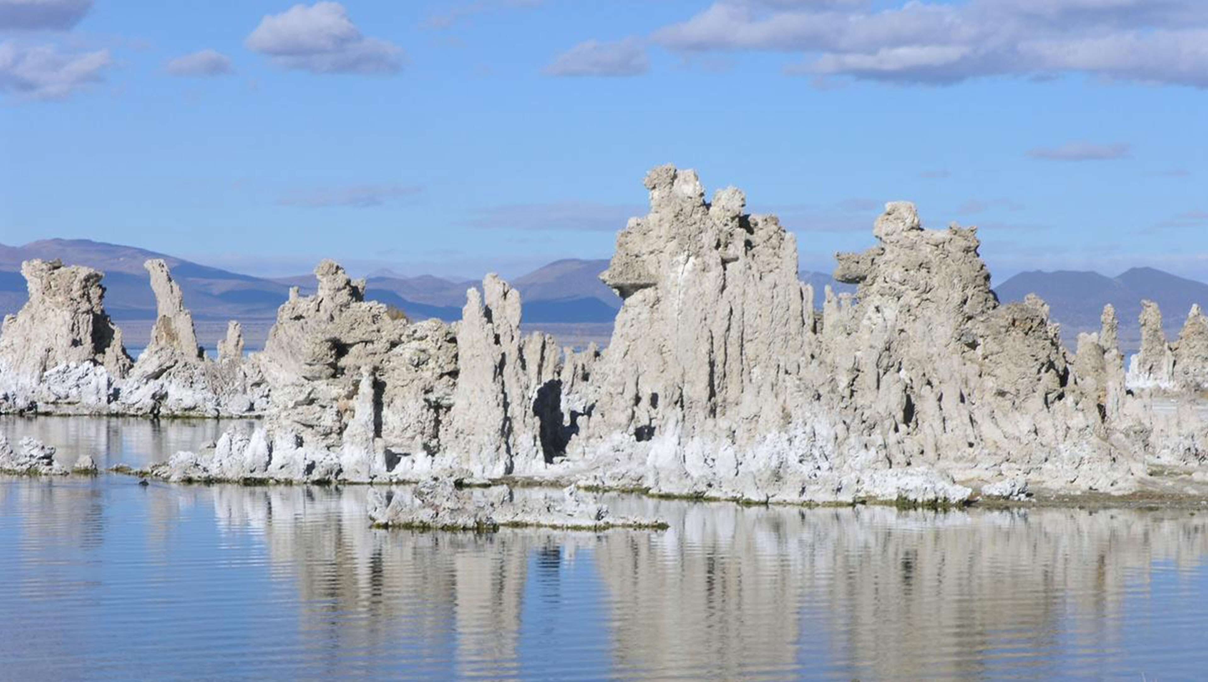 A landscape of unique rock formations surrounded by a calm body of water, with mountains in the background.