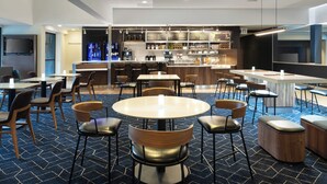 Un hall d’hôtel moderne avec des tables rondes, un bar et des espaces pour s’asseoir.