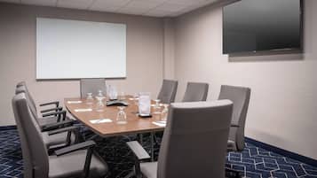 Una sala de conferencias con una gran mesa, seis sillas, una pantalla de proyector y un televisor de pantalla plana.