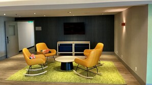 A modern lounge area with a round table, four rocking chairs, and a television screen on the wall. - Spark by Hilton Montreal Brossard (Brossard)