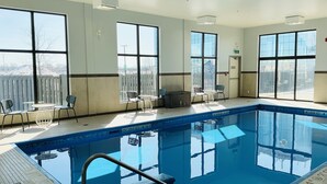 An indoor swimming pool with clear windows, a tiled floor, and a few chairs and tables. - Spark by Hilton Montreal Brossard (Brossard)