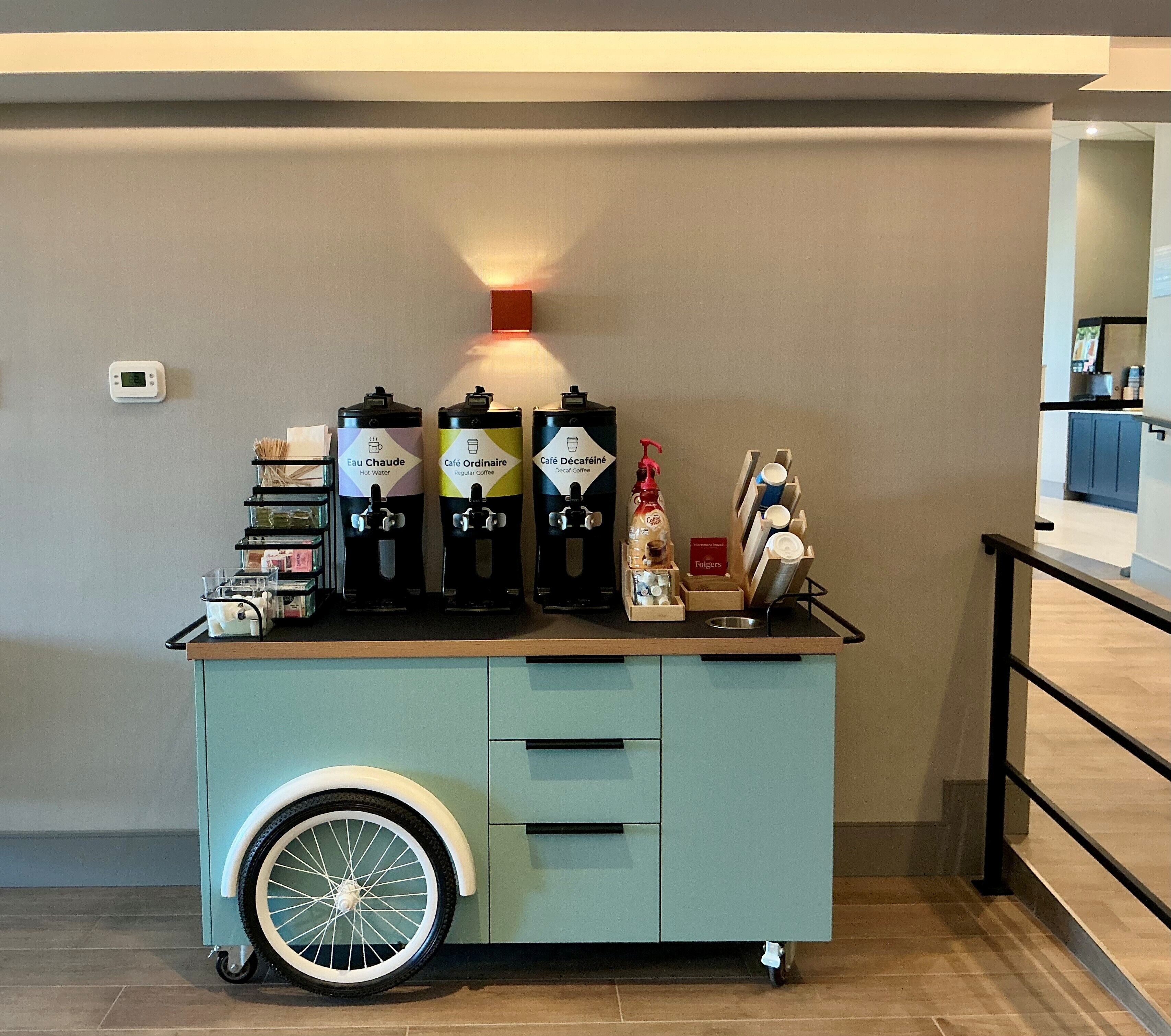 A self-service coffee station with hot water, regular coffee, and decaffeinated coffee options.
