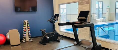 A fitness room with a treadmill, exercise balls, and a pool view.