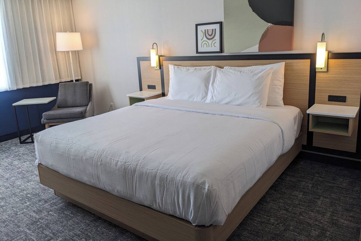 A hotel room with a large bed, bedside tables, a chair, a lamp, and a painting on the wall.