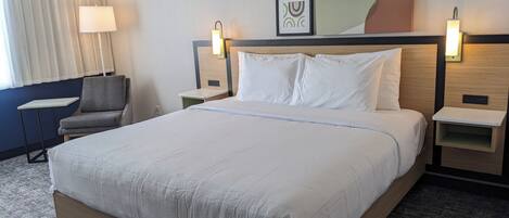 Un cuarto de hotel con una cama grande, mesitas de noche, una silla, una lámpara y un cuadro en la pared.