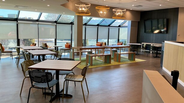 A modern dining area with tables and chairs, large windows, and a flat-screen TV on the wall. - Spark by Hilton Montreal Brossard (Brossard)