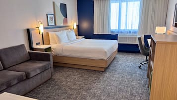 Una habitación de hotel con cama, escritorio, silla, sofá y ventana con cortinas.