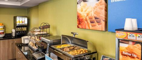 A breakfast bar with various food options, a waffle maker, and a Better Batter advertisement.
