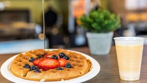 A waffle topped with strawberries and blueberries, a glass of a light-colored beverage, and a potted plant in the background. - Comfort Inn Winnipeg Airport (Winnipeg)